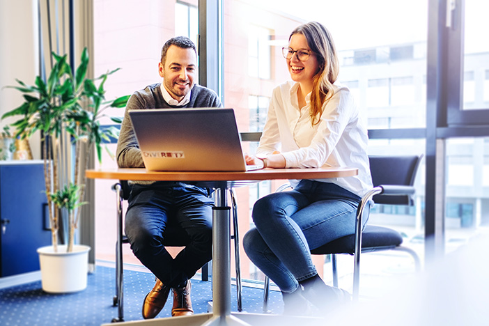 Zwei Mitarbeiter sitzen am Tisch und schauen gemeinsam auf den Laptop