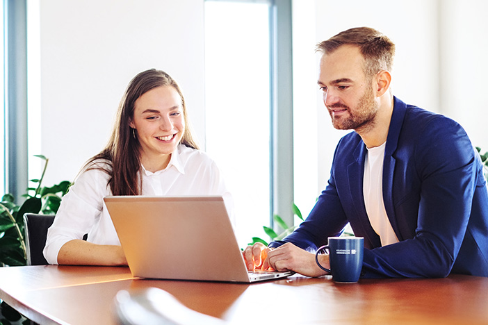 Zwei Mitarbeiter sitzen am Tisch und schauen gemeinsam auf den Laptop