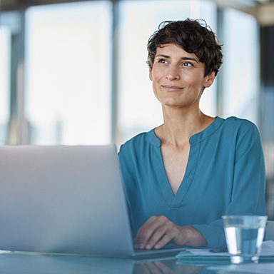 Frau am Laptop blickt in die Ferne.