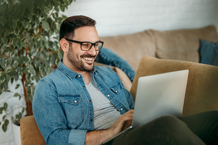 Mann sitzt auf der Couch mit Laptop auf dem Schoß
