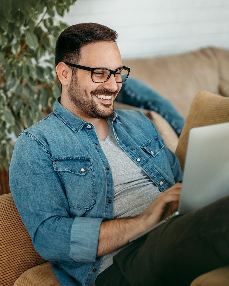Lächelnder Mann sitzt auf dem Sofa mit Laptop auf den Beinen